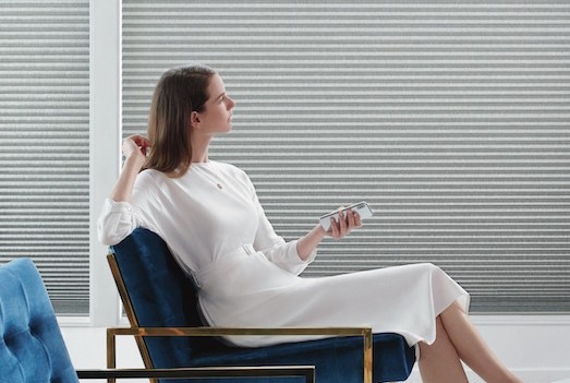 Women in white dress siting on a blue chair using her phone to operate her shades.